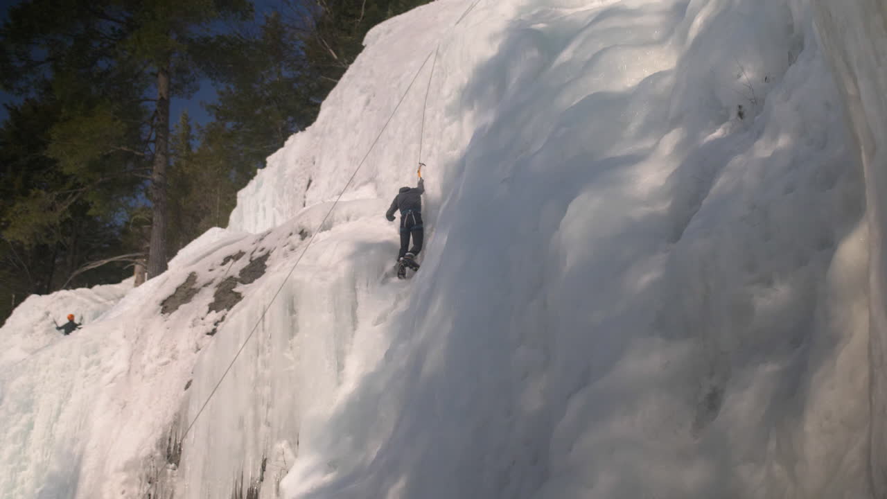 amplio ángulo de visión de un escalador que asciende a la cumbre de una pared de hielo congelado