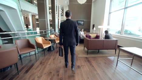 businessman holding a briefcase and entering a hotel hall while talking on the phone