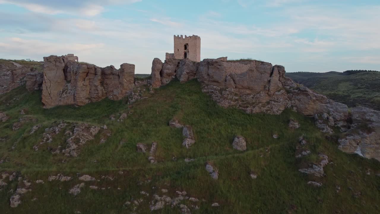 Aerial view of lush green crop fields with an ancient hilltop castle in the background near Aranjuez, Spain. Scenic rural landscape with medieval architecture.