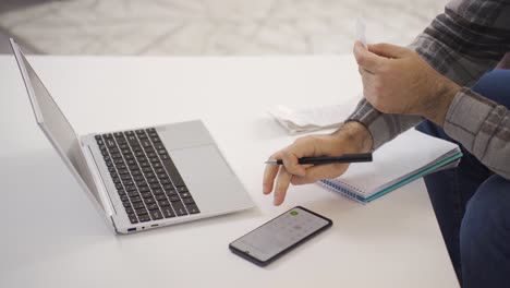 mature man calculating online loan debt payments and shopping receipts.