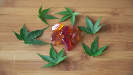 push in to cbd gummies in pile surrounded by circle of marijuana leaves on light wood tabletop