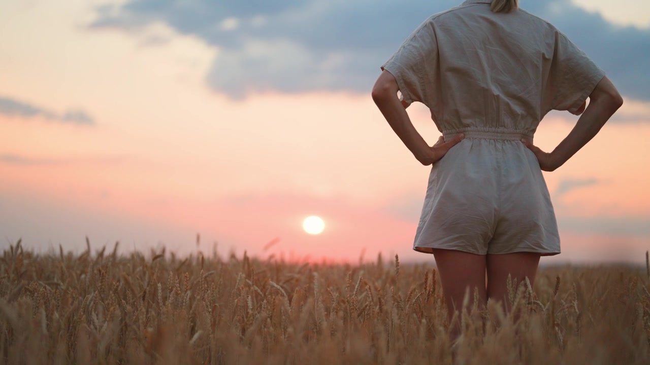 Young Woman Standing in Wheat Field at Sunset