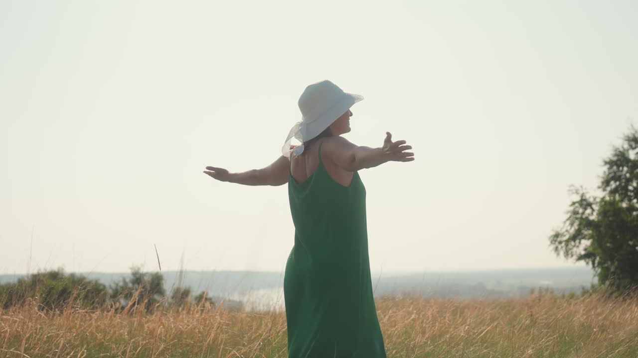 excited woman in green dress spreads arms wide dancing freely in open field near lush trees under clear sky, celebrating adventure and joy surrounded by tall grass