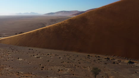 drone shot around a sand dune while the wind dusts sand over it, sunny day in the namib desert, namibia