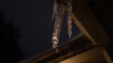 Backlit-Melting-Icicle-hanging-from-roof,-dripping-in-slow-motion