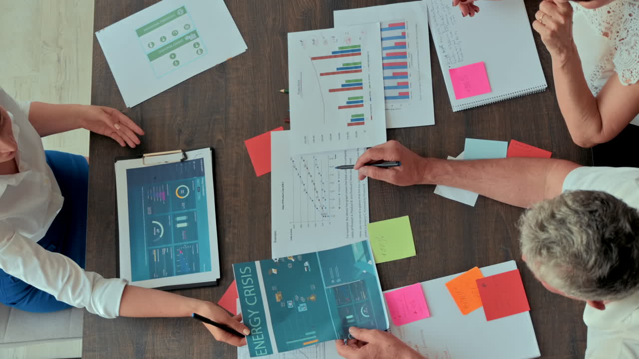 Three coworkers analysing energy crisis graphs at a desk in an office