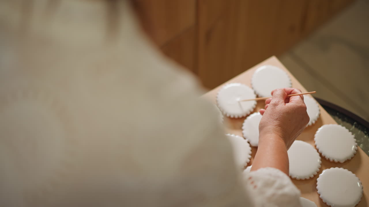 Caucasian baker arranging iced pies from overhead, overshoulder view of gentle hand placement on round tarts, warm kitchen light, homely rhythm and careful finishing before serving