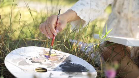 close-up of a hand mixing paints on an artist's palette outdoors
