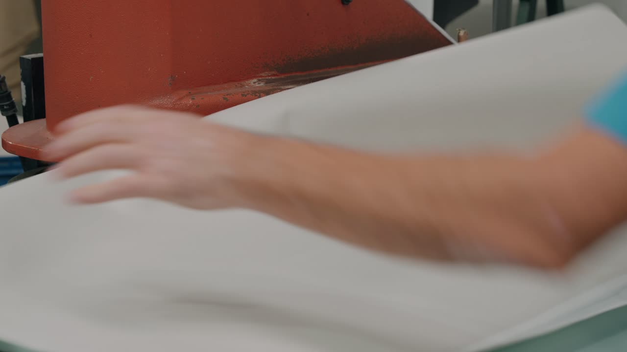 Trabajador cortando láminas textiles con equipos de prensa industrial