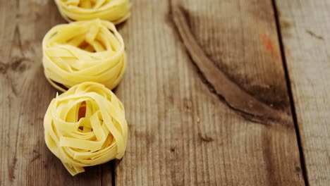 Roll-of-tagliatelle-pasta-following-others-on-wooden-table-background