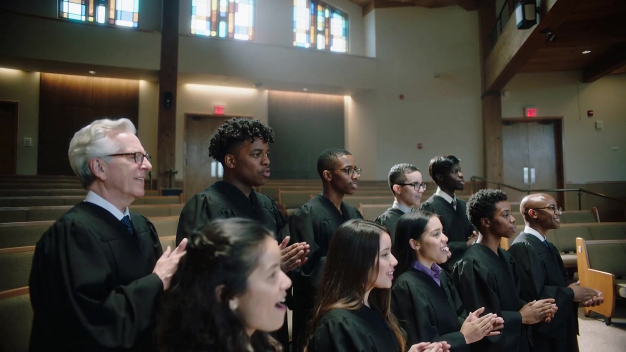 Singing choir in black robes moving to clapping after song starting in church with stained glass