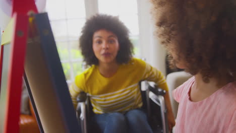 mother in wheelchair watching daughter having fun drawing picture on whiteboard at home