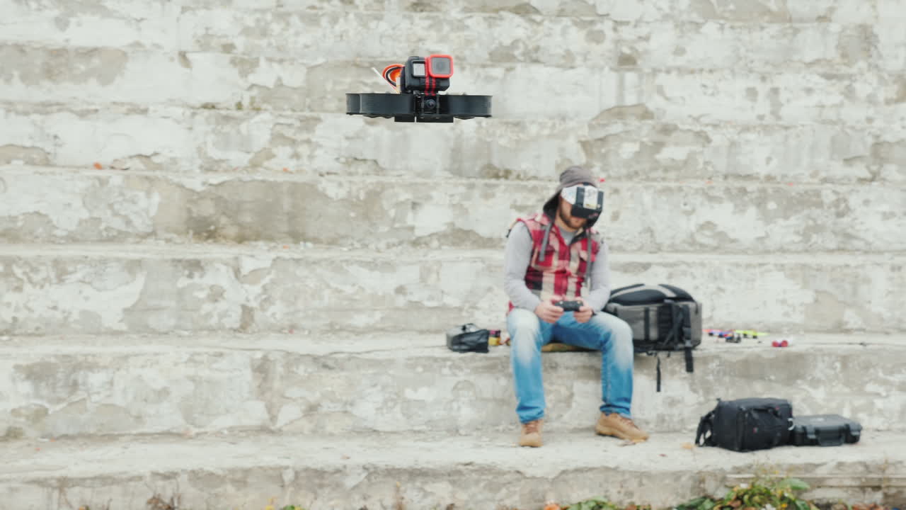 원격 측정 기능이 있는 헬멧을 쓴 남자가 그 앞에서 날아가는 드론을 제어합니다.