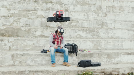 a man in a helmet with telemetry controls a drone that flies in front of him