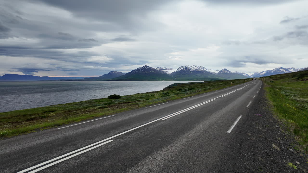 Dynamic footage showcasing two cyclists pedaling along Road 82 near Dalvik, Iceland, backdrop of northern Iceland's breathtaking coastal and mountain scenery.