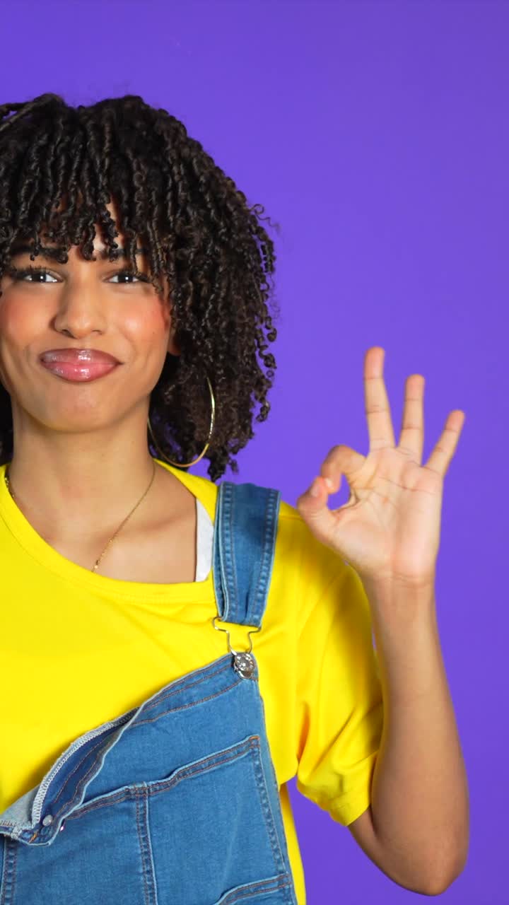 Woman with curly hair giving ok sign in front of purple background