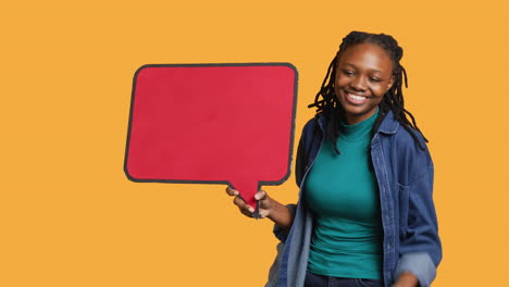 smiling woman holding red speech bubble sign, studio background