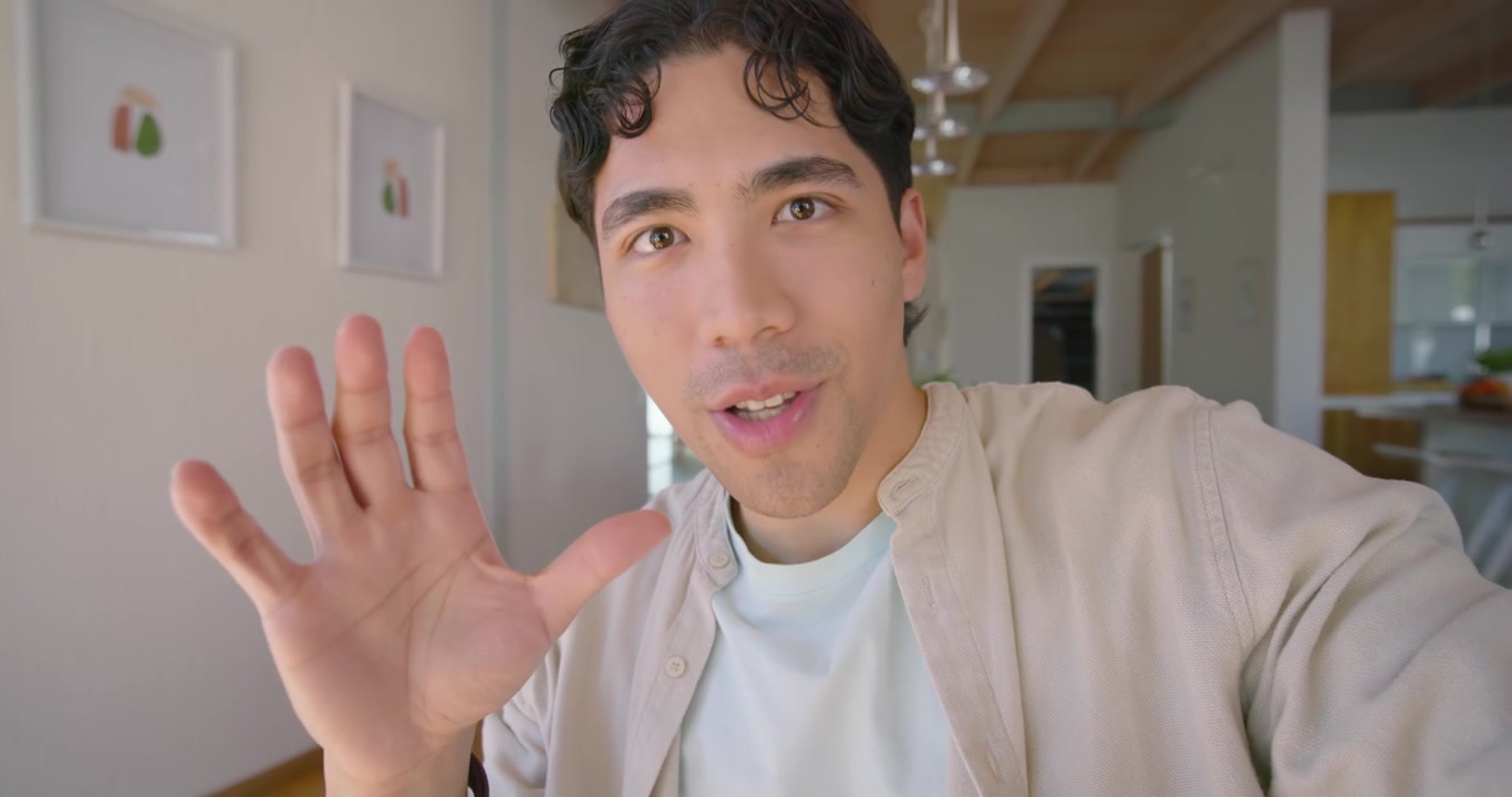 Uomo afroamericano che tiene in mano uno smartphone, condivide consigli in una casa open space, indossa una camicia beige.