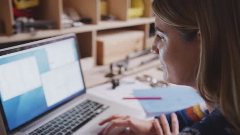 primer plano de una ingeniera en el taller usando una computadora portátil y tomando notas sobre el plan para la bicicleta