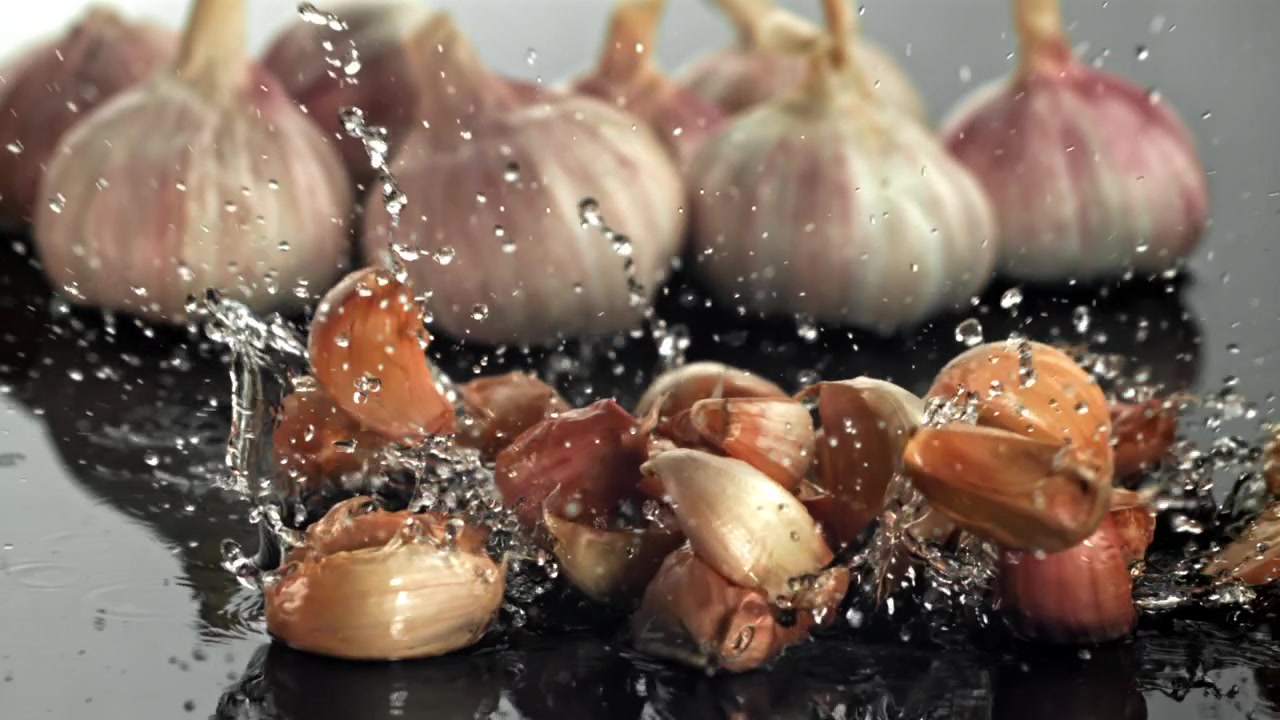 Spicchi d'aglio freschi che cadono e schizzano nell'acqua in slow motion