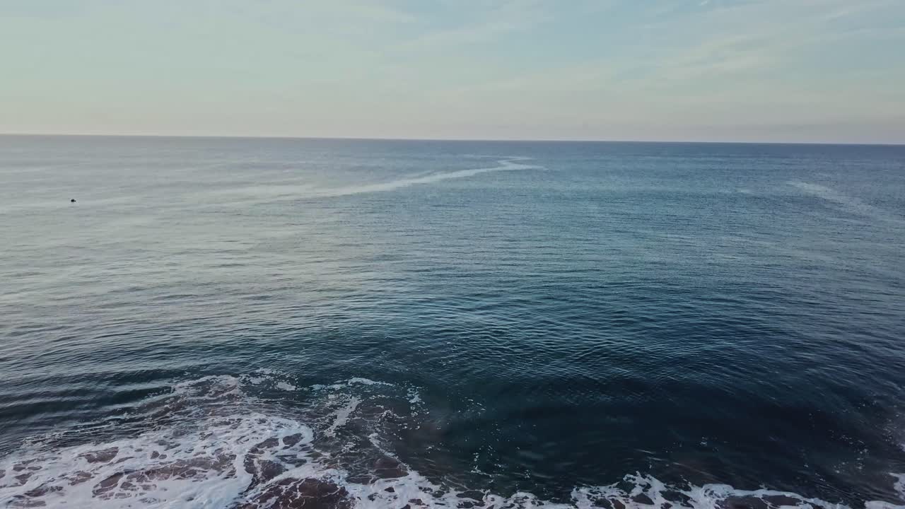 aerial low angle dolly out establishing shot of empty blue ocean, wide angle