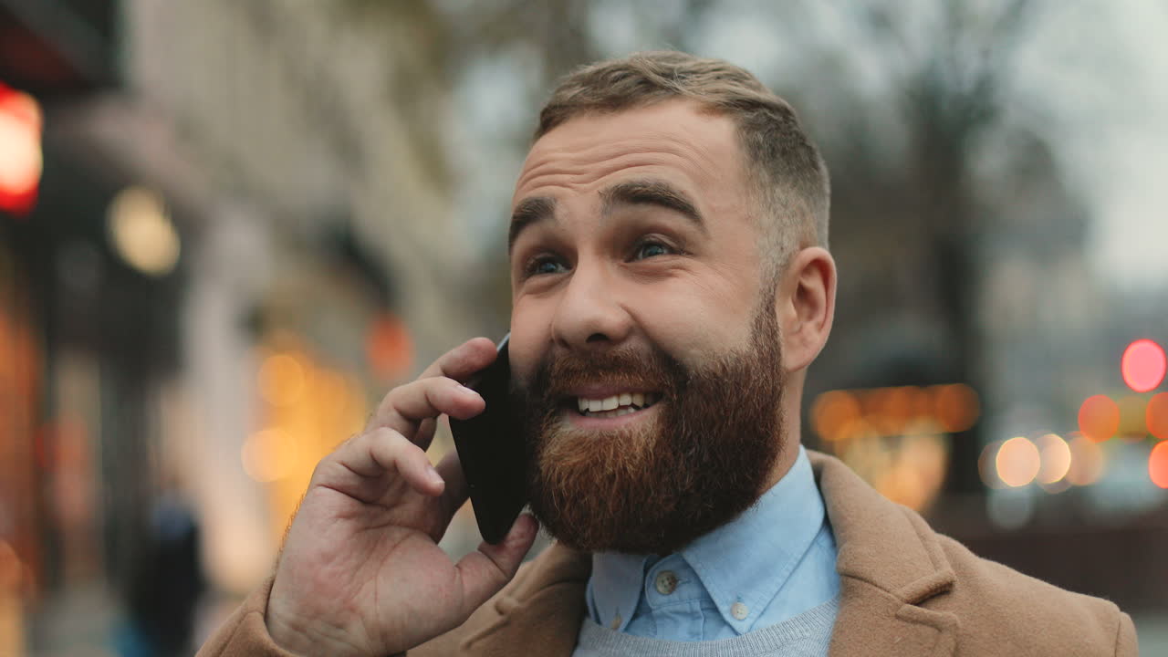 vista cercana del hombre de negocios caucásico con barba hablando por teléfono y sonriendo en la calle en otoño