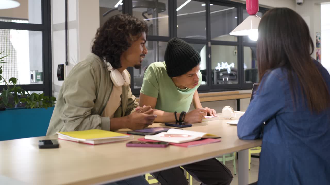 Diverse coworkers reacting to left man speaking, leaning over laptop and notes, celebrating success