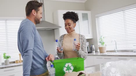 video de una feliz pareja diversa recolectando botellas de plástico para reciclar en casa
