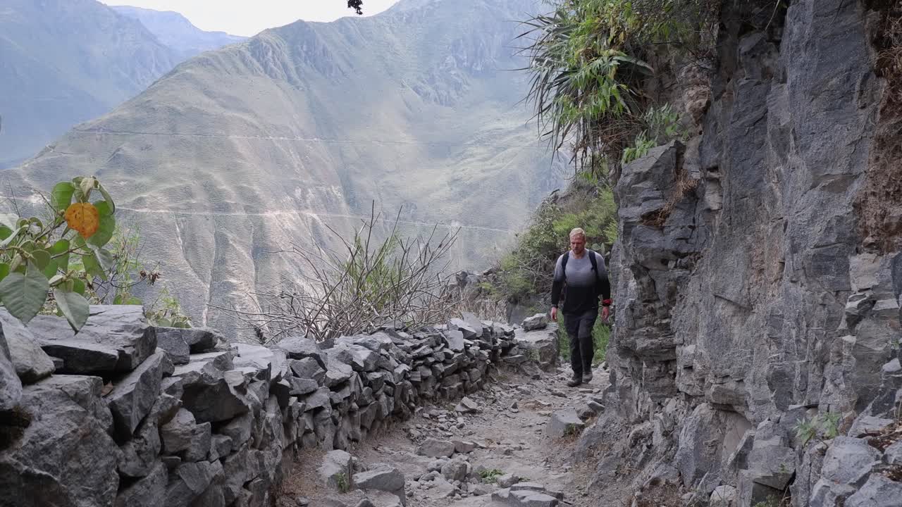 un joven sube por un estrecho sendero rocoso en el cañón de colca, perú.