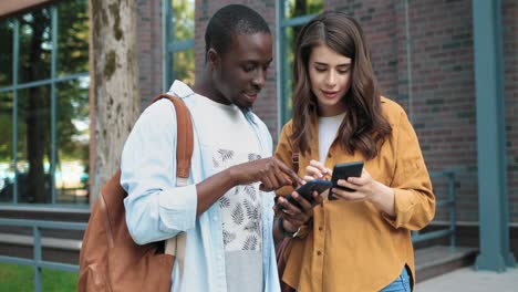 camera zooming on a caucasian woman and african american man discussing about something looking at smartphone in the street near the university