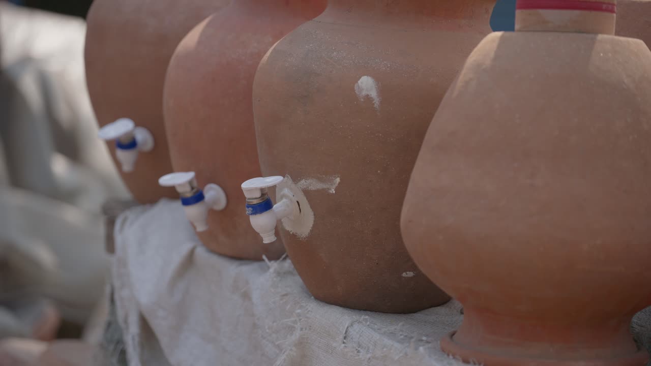 Fileiras de potes de água tradicionais de barro de terracota, equipados com torneiras de plástico modernas, expostos por vendedores ambulantes na Índia. Ideal para documentários de viagem e conteúdo cultural.