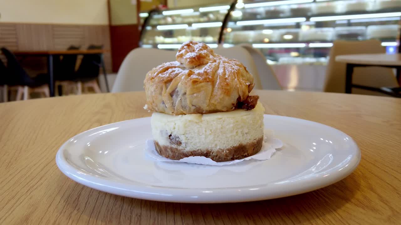 Zoom out of layered cheesecake with crispy puff pastry topping, served on a white plate