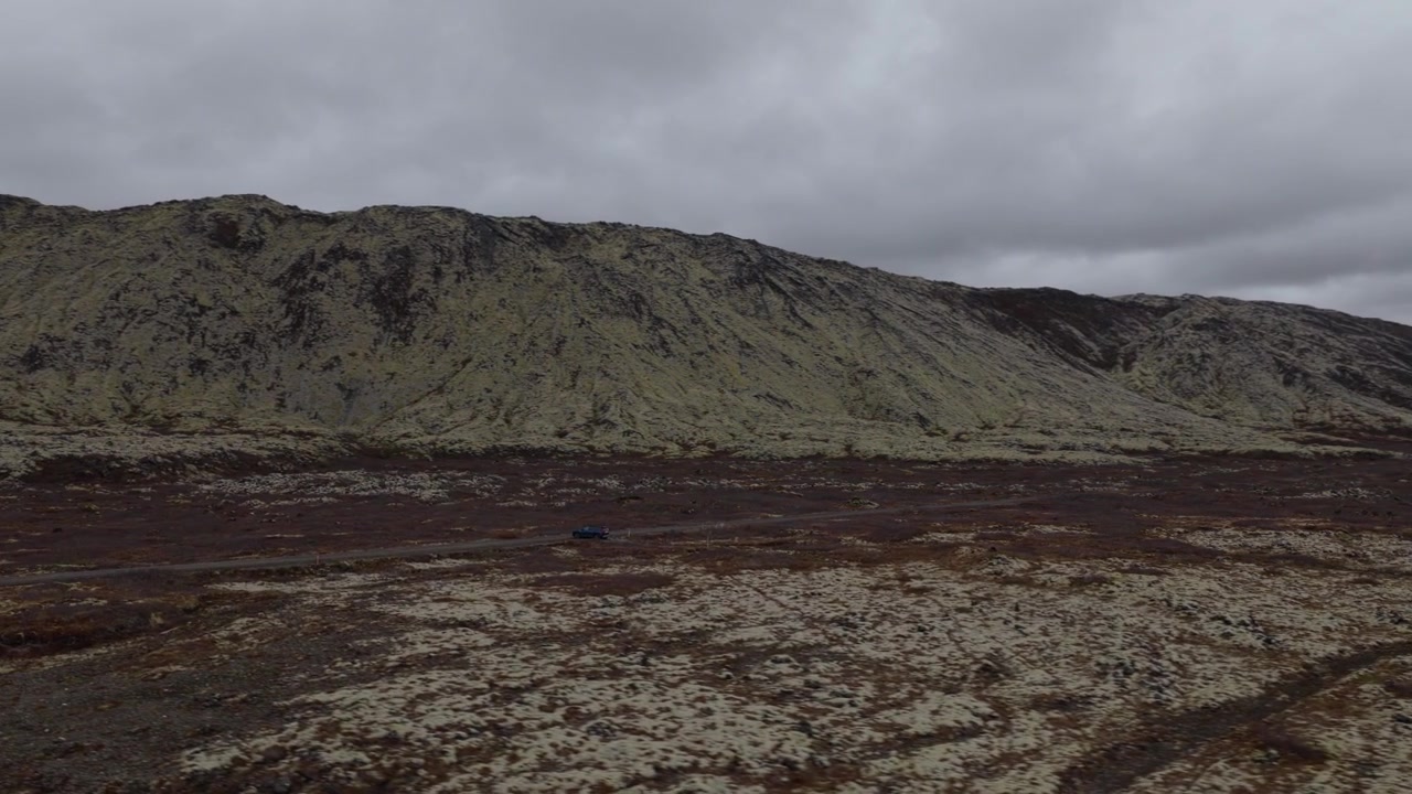 Volcanic ridge rises above barren mineral terrain at Seltun in the Krysuvik area of Reykjanes, Iceland, with sparse vegetation covering the rugged ground, aerial orbit.