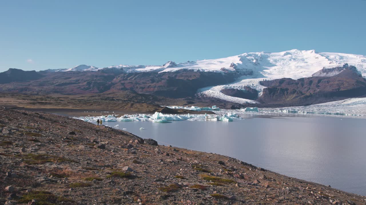 Hikers walking on trail along Fjalls&aacute;rl&oacute;n glacier lake in Iceland
