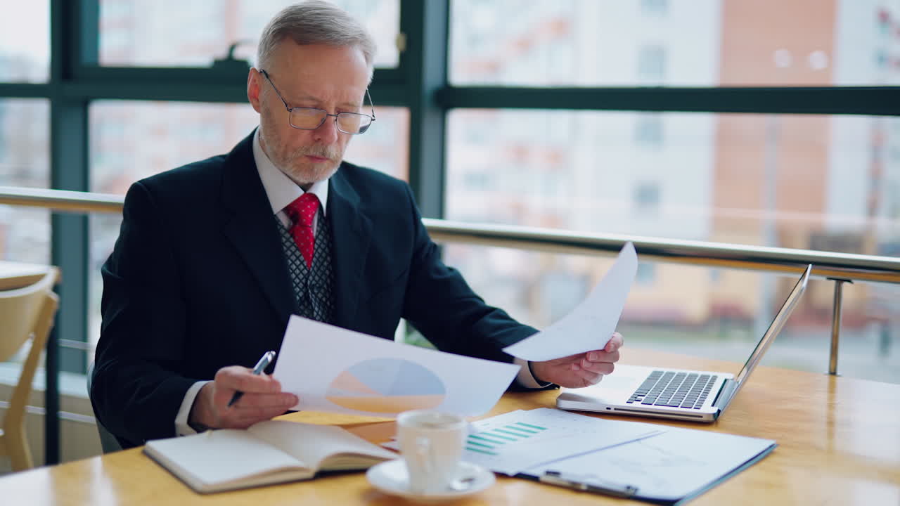 Thoughtful businessman is reading important business papers, video in front of the window with city view. Video of business process.