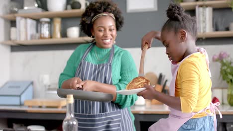 Happy-african-american-mother-and-daughter-frying-pancakes-in-kitchen,-slow-motion