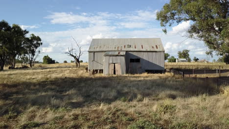 Aerial-footage-moving-through-agricultural-land,-past-a-barbed-wire-fence-and-an-old-barn-made-from-corrugated-metal,-on-a-dry,-sunny-day