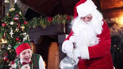 happy female elf looking at santa pouring water. preparation for drinking tea with cookies on christmas background