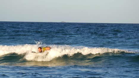 bearded male surfer paddling surfboard, riding ocean waves, smiling, happy expression