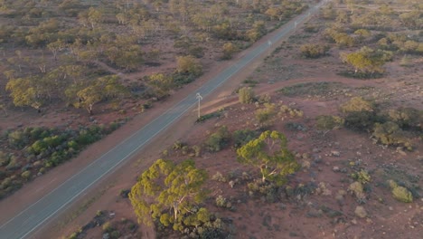 Overhead-clip-over-lorry-with-3-wagons-driving-along-straight-road,-through-remote-desert-landscape