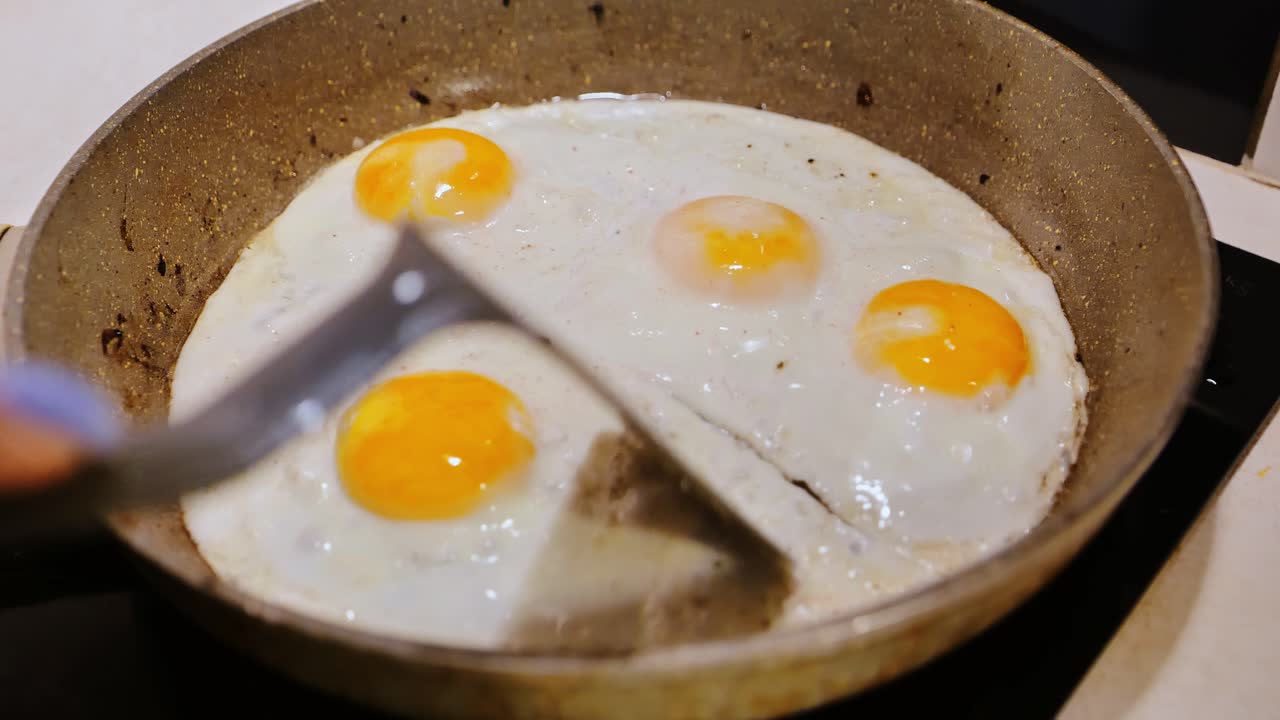 Telur goreng yang baru saja digoreng dipisahkan perlahan dengan spatula dalam pencahayaan dapur yang nyaman