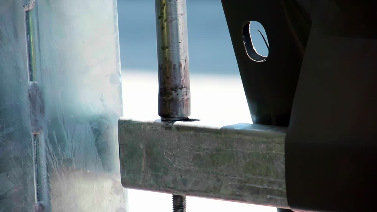 Close up slow motion footage of a metal locking pin and galvanized steel bracket being aligned and secured during industrial assembly or construction installation