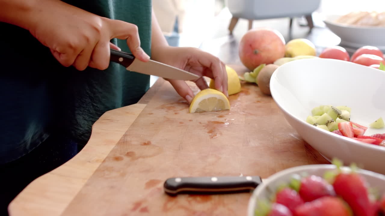 Cutting lemon slices on wooden board, person preparing fresh fruit salad