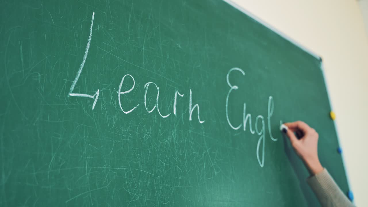 Close-up of a hand with a chalk writing the word English. Woman's hand holding chalk and writing the words Learn English on the green board.