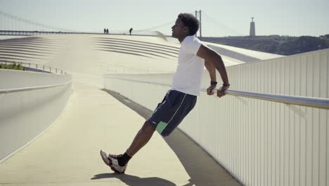 Side-view-of-sporty-young-man-doing-push-ups-near-metal-railing