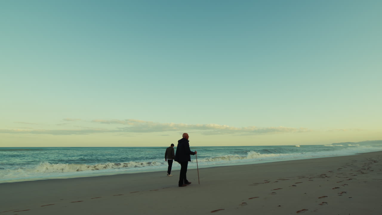 Near the stormy ocean waves, two men are walking relaxed