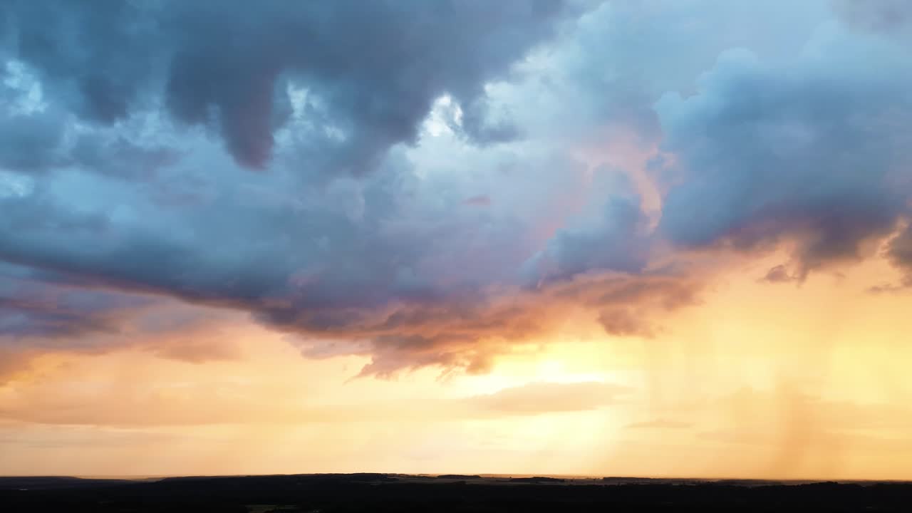 Orange sunset sky with dark stormy rainfall clouds, aerial panoramic view