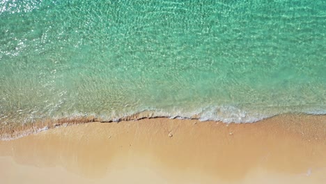 Sea-texture-with-crystal-emerald-water-of-seashore-waving-on-white-sand-of-exotic-beach-on-a-bright-sunny-morning,-copy-space