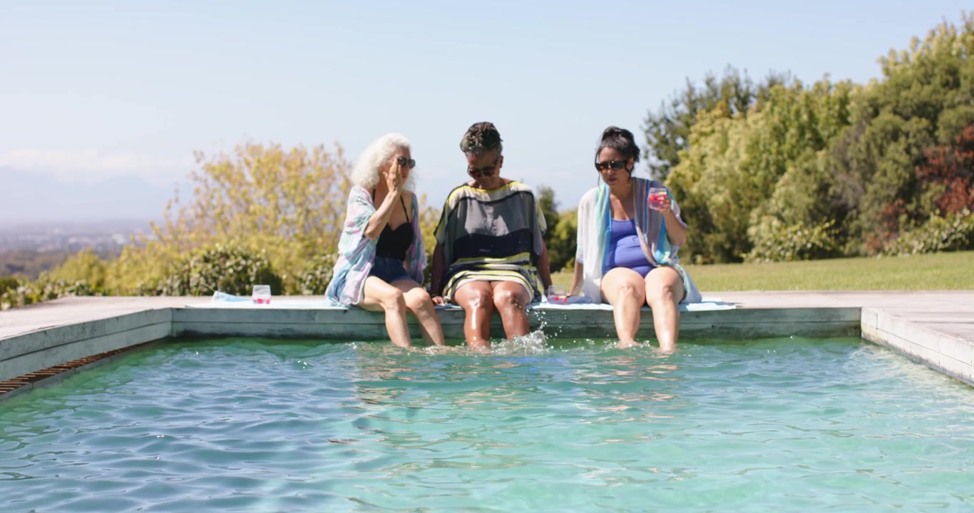 Diverse women at hillside pool, central shifting feet and kicking, right sipping clear cup, cooling