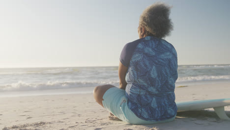 Happy-senior-african-american-woman-sitting-at-beach-at-beach,-in-slow-motion